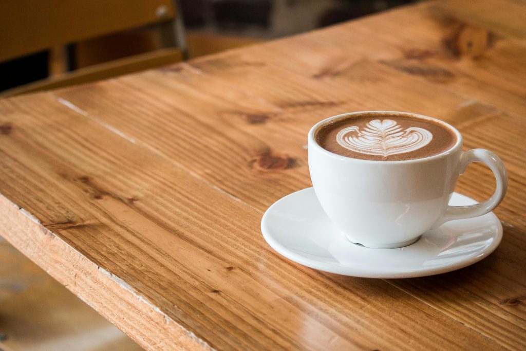 Cup of coffee with latte art on a wooden table, illustrating caffeine overload as one of the worst foods for hormone health due to its impact on cortisol and energy balance.