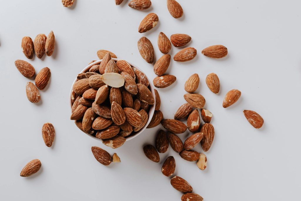 Bowl of almonds with scattered nuts on a white background, showing one of the foods to balance hormones naturally.