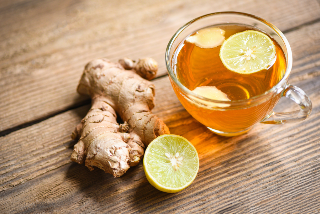 Glass cup of warm ginger lemon tea with fresh ginger root and sliced lemon on a wooden table, illustrating a natural drink that supports liver function and hormone balance.