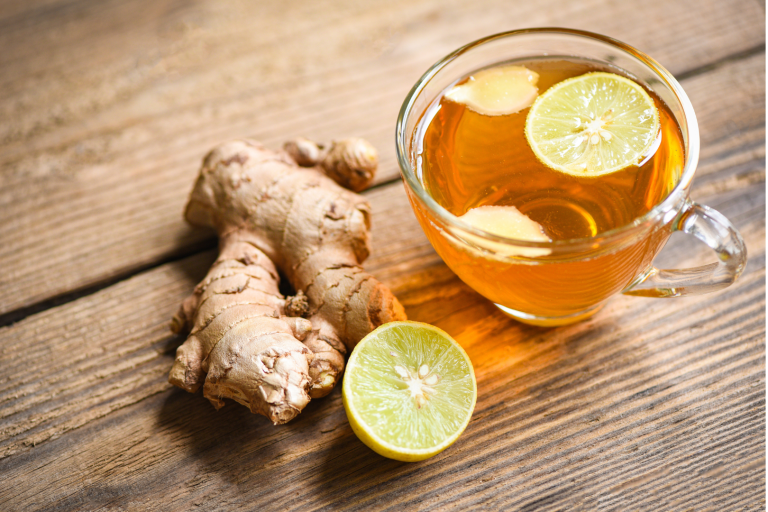 Glass cup of warm ginger lemon tea with fresh ginger root and sliced lemon on a wooden table, illustrating a natural drink that supports liver function and hormone balance.