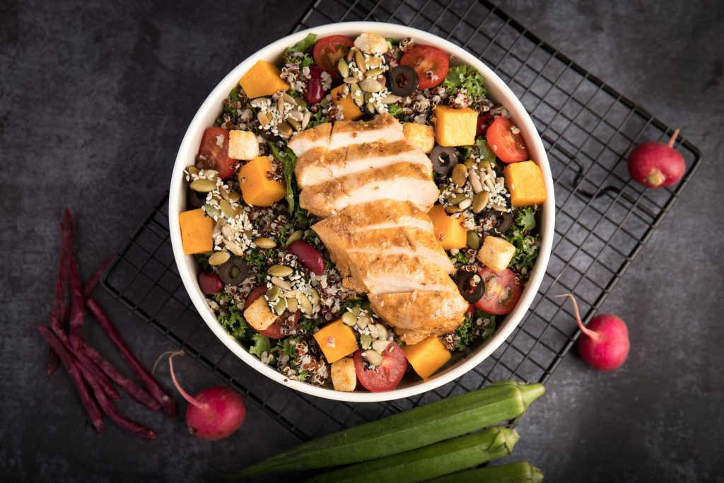 Bowl of grilled chicken over a colorful quinoa and vegetable salad, used as an example meal in a hormone balance diet plan for women.