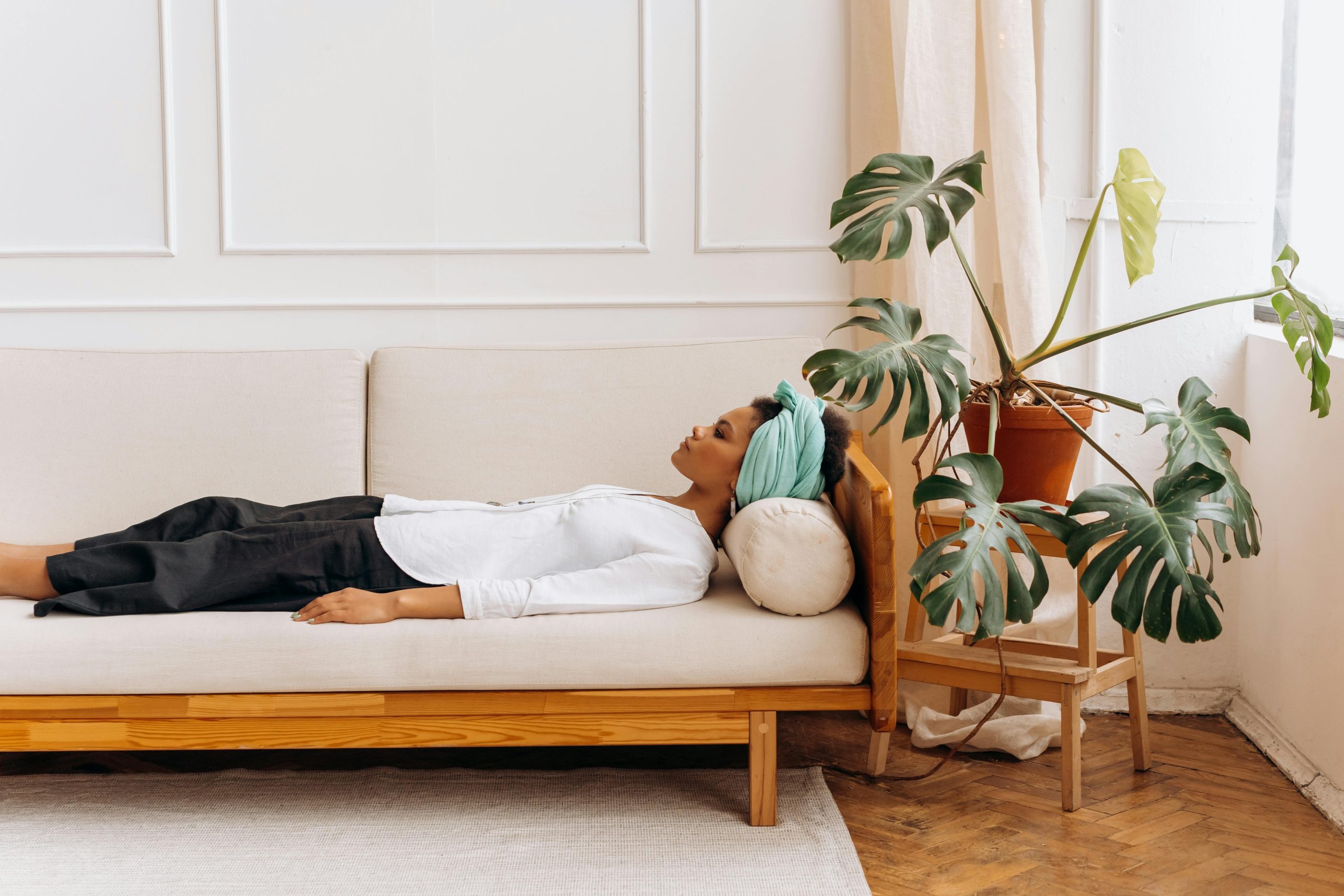Woman resting quietly on a beige sofa beside a green houseplant, reflecting calm fatigue and natural balance — representing signs of progesterone deficiency after 40.