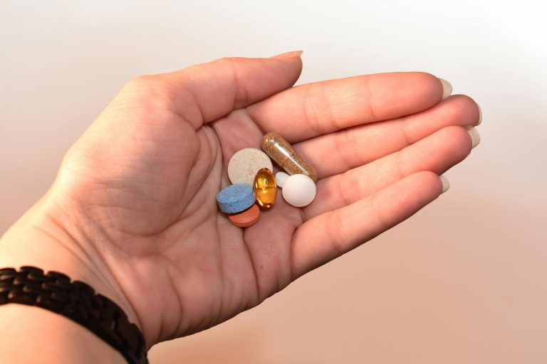 Woman’s hand holding a variety of supplement pills and capsules, illustrating supplements for hormone balance women can use for midlife wellness.
