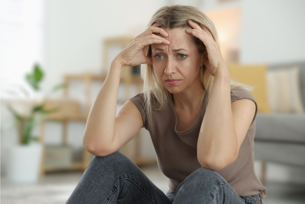 Woman in her 40s sitting with her hands on her head, looking stressed, used to illustrate how cortisol spikes relate to sugar and hormones in midlife.