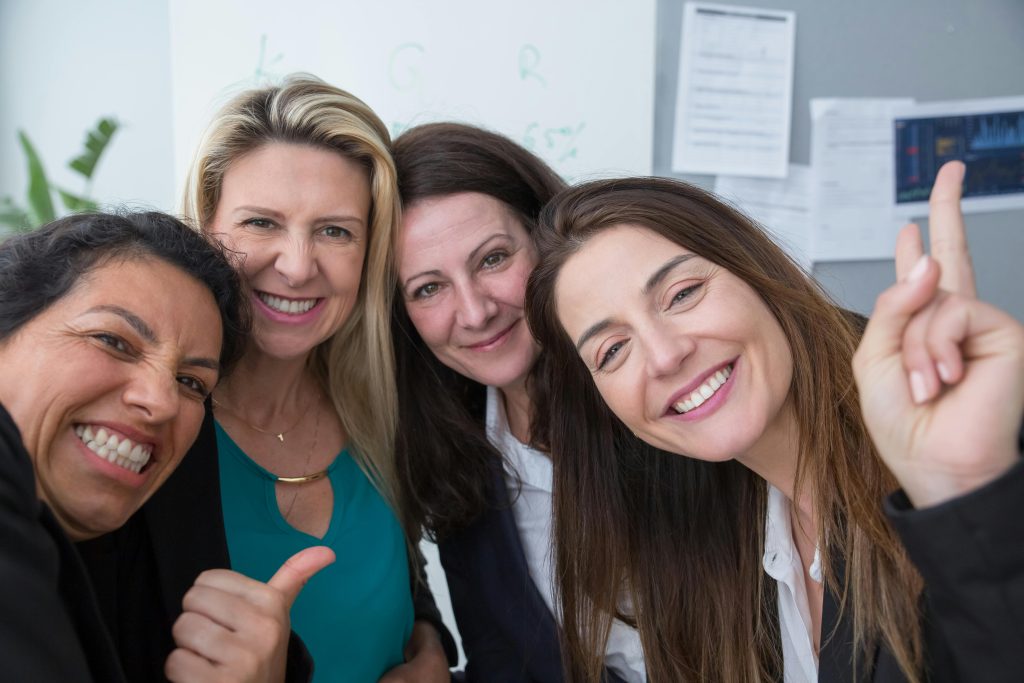 Group of smiling women over 40 standing close together and laughing, representing connection and confidence in midlife wellness.