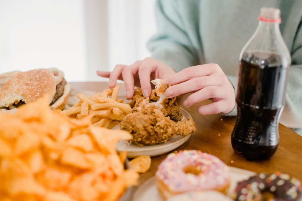 Person eating fried chicken, French fries, donuts, and drinking soda — a visual example of the worst foods for hormone health due to their impact on inflammation, blood sugar, and hormone balance.