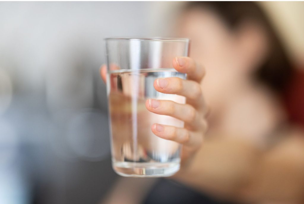 Hand holding a glass of water in the morning, representing hydration before coffee as part of a morning routine for hormone balance.