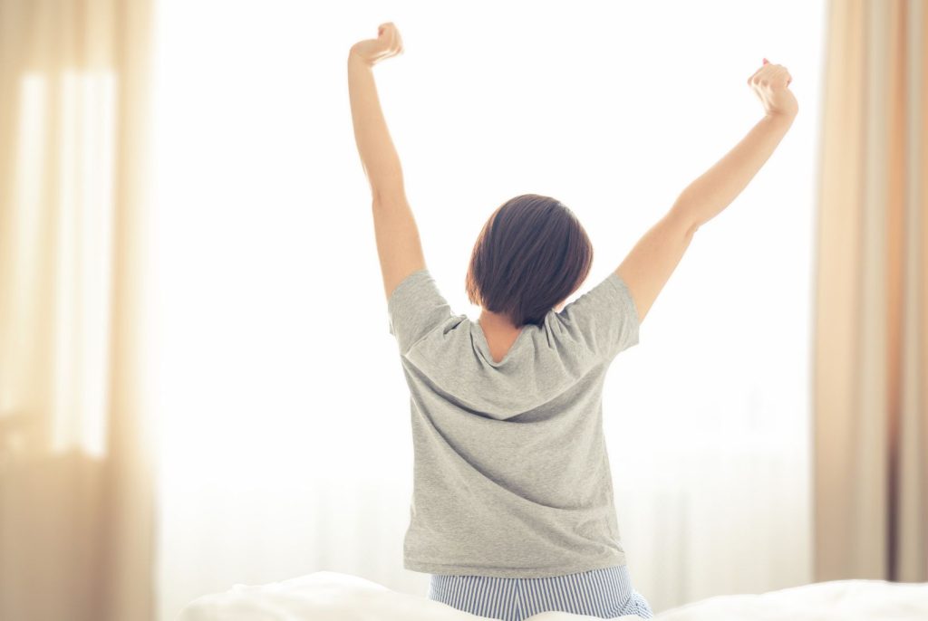 Woman stretching with arms raised in morning light, representing a gentle morning routine for hormone balance that supports energy and mood after 40.