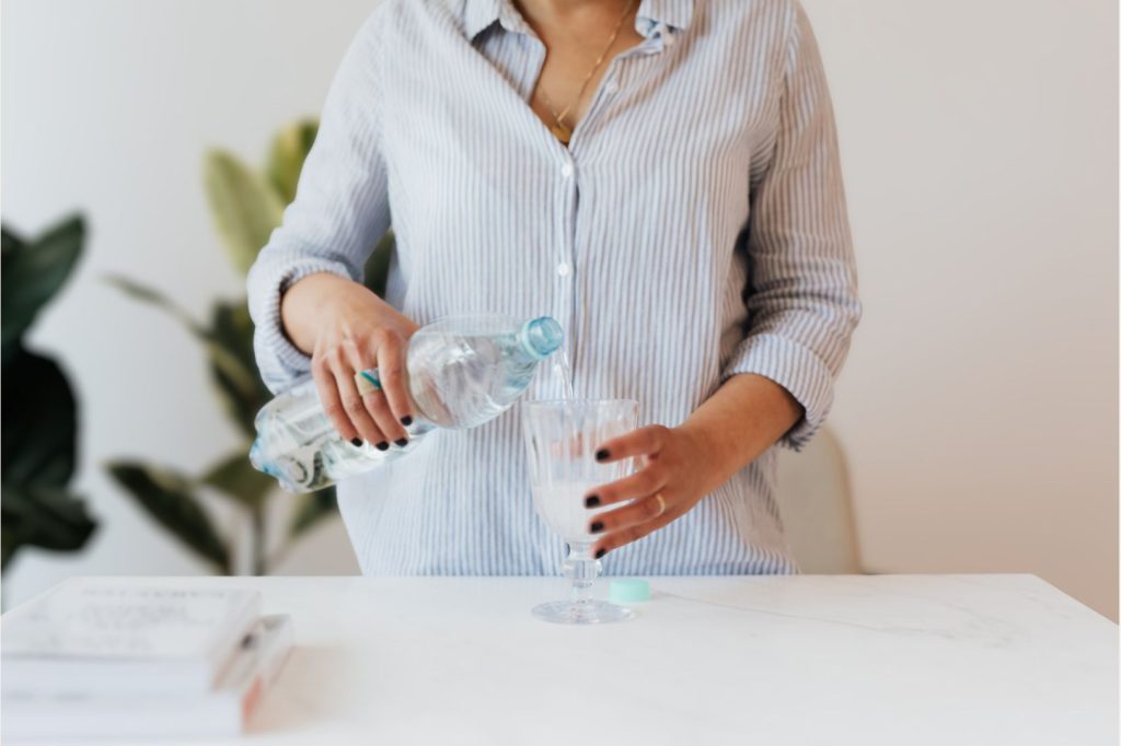 Woman pouring water into a glass in a bright kitchen, illustrating the importance of hydration for liver detox and hormone balance.
