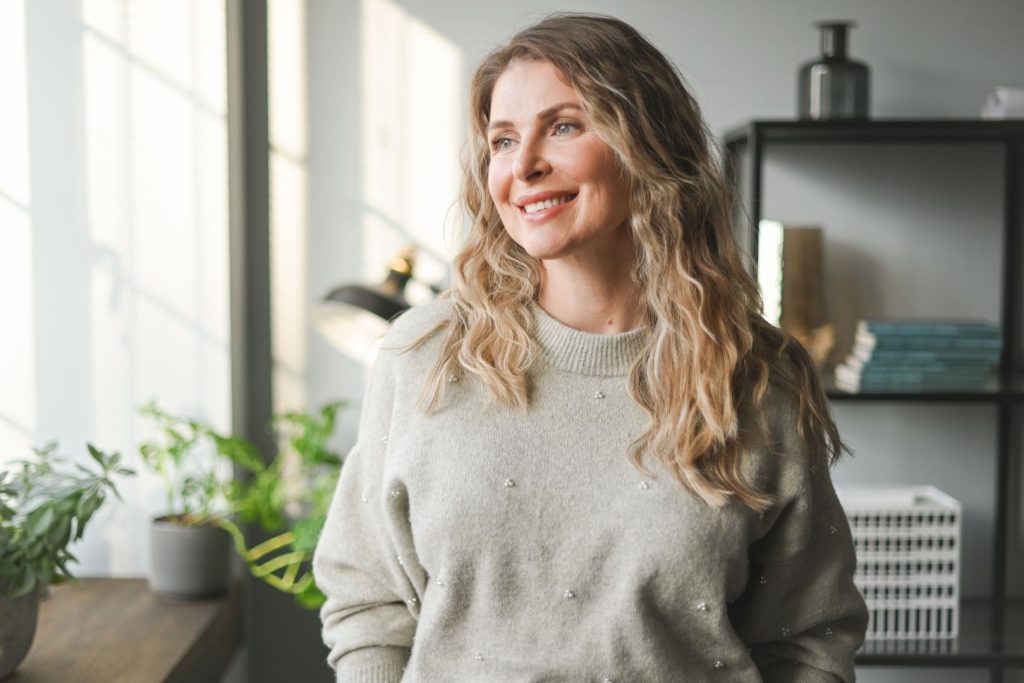 Woman over 40 standing near a window in soft natural light, representing hormone imbalance in women over 40 and midlife wellness.
