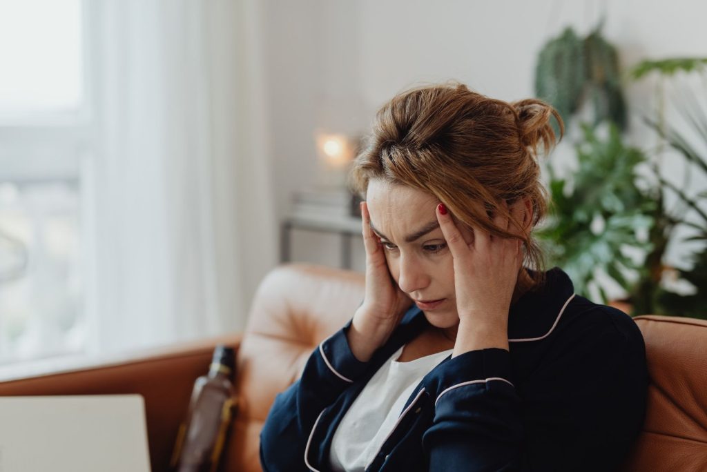 Woman over 40 sitting on a couch holding her head, showing stress and overwhelm related to hormone imbalance in women over 40.