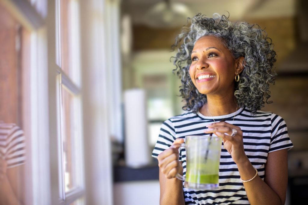 Woman over 40 holding a warm drink by a window, representing how to balance hormones naturally through daily habits and lifestyle support.