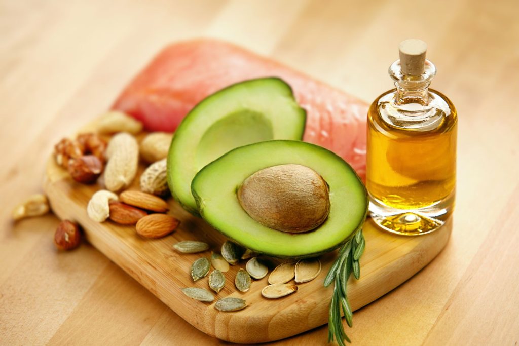 Avocado, salmon, nuts, seeds, and olive oil on a wooden board representing healthy fats that support hormone balance after menopause.