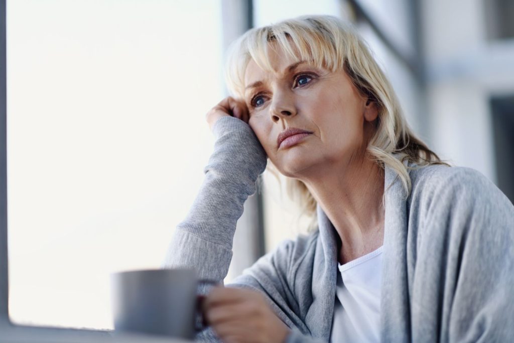 Woman over 50 sitting by a window in a reflective moment, representing hormone imbalance after menopause