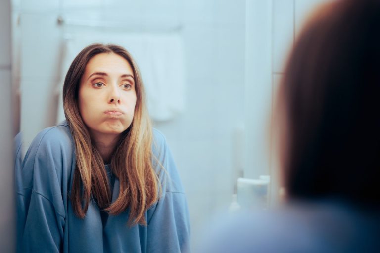 Woman in her 40s looking at herself in the mirror, reflecting on hormone changes during perimenopause and what to expect.