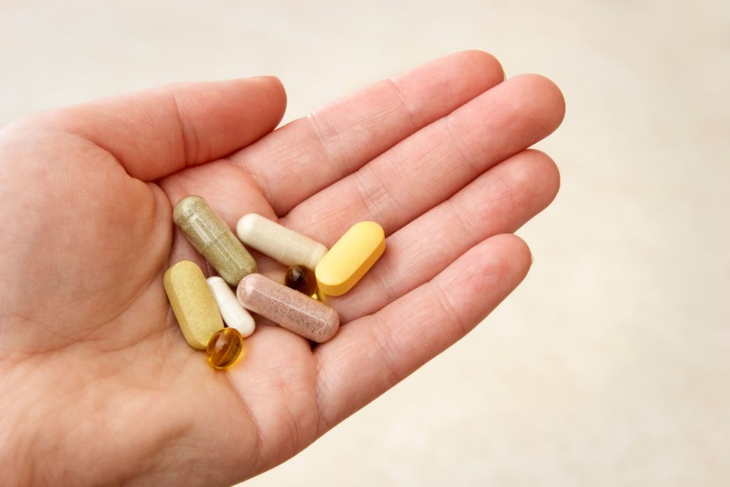 Hand holding various supplements that may support hormone health and overall wellness after menopause.