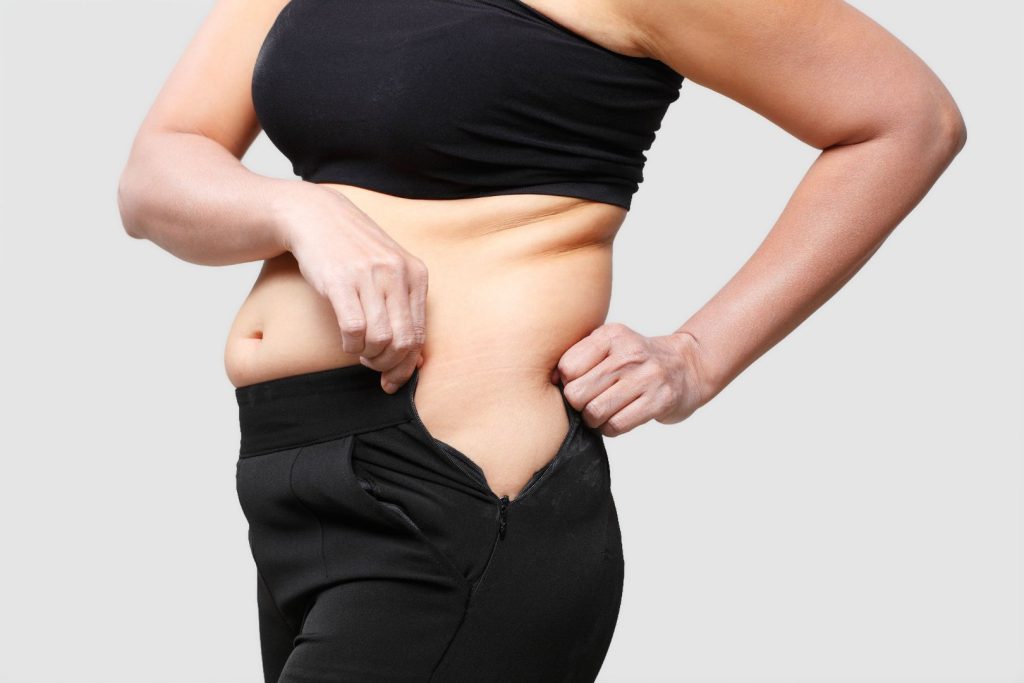 Woman holding belly fat and struggling to zip pants, illustrating hormone imbalance weight gain and belly fat after 40.