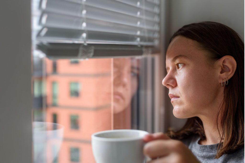 Woman over 40 holding coffee and looking thoughtful by window during hormone imbalance mood swings